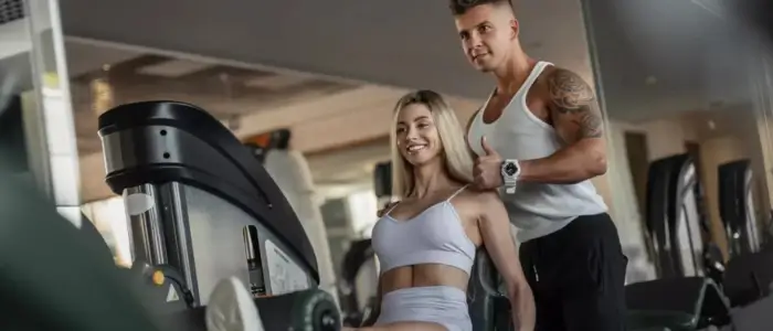 a man, and woman, in gym tank tops training at the gym