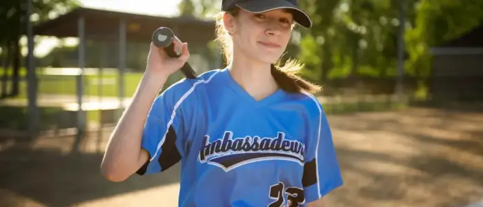 a girl in a custom women baseball jersey holding a bat