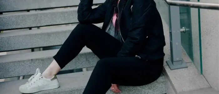 woman wearing bomber jacket sits on stairs