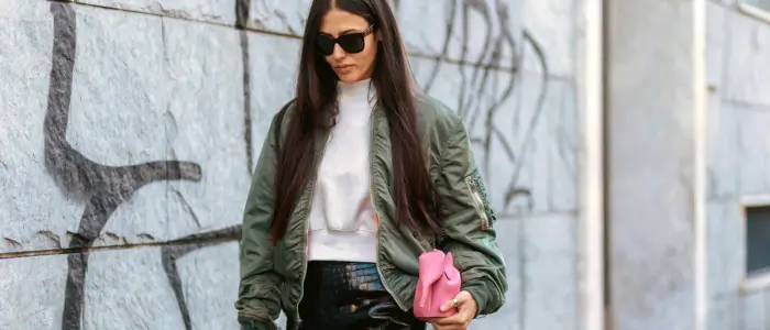 a woman wearing black pants and a green bomber jacket 