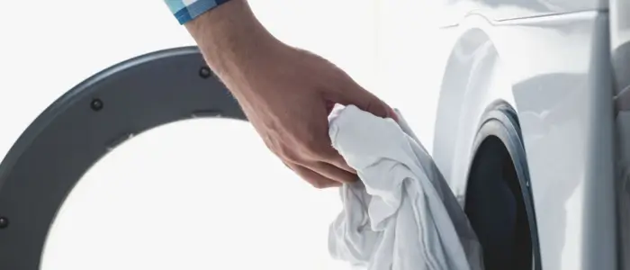 men carefully places a white nylon cloth into a washing machine, preparing for a wash cycle to prevent shrinking